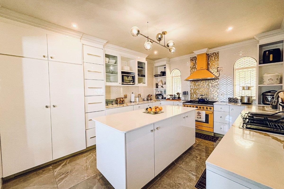 Modern kitchen featuring a central island, white cabinetry, quartz countertops, a vibrant yellow range with matching extractor, and elegant tiled flooring.