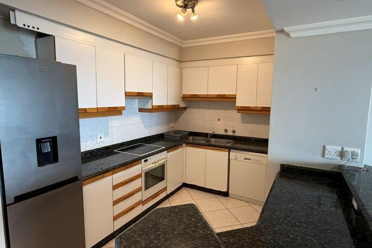 Functional kitchen featuring white cabinetry, dark granite countertops, integrated oven and hob, and a breakfast bar area with tiled flooring.