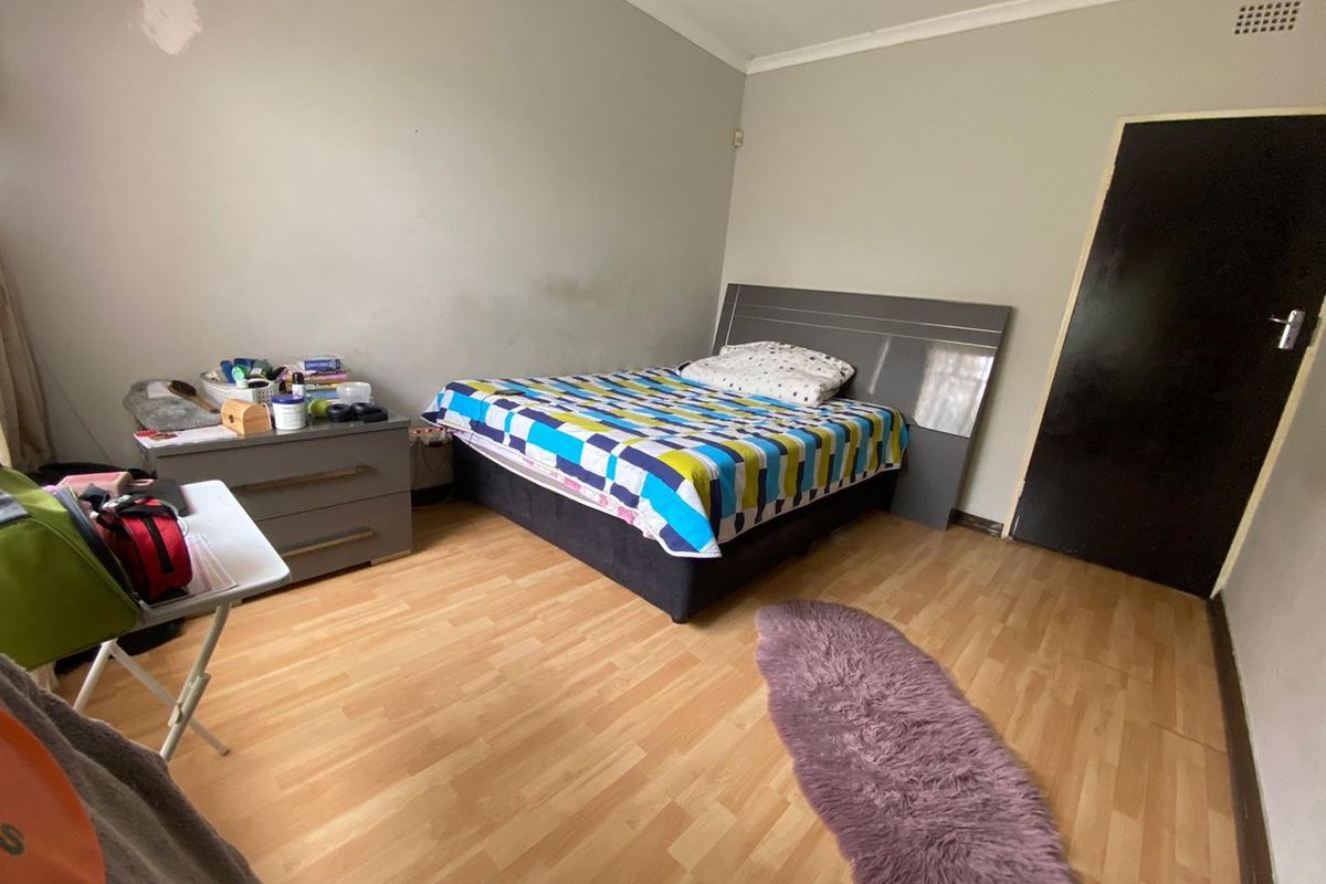 A bedroom featuring laminate flooring and coved ceilings, currently requiring cosmetic updates to the wall finishes.