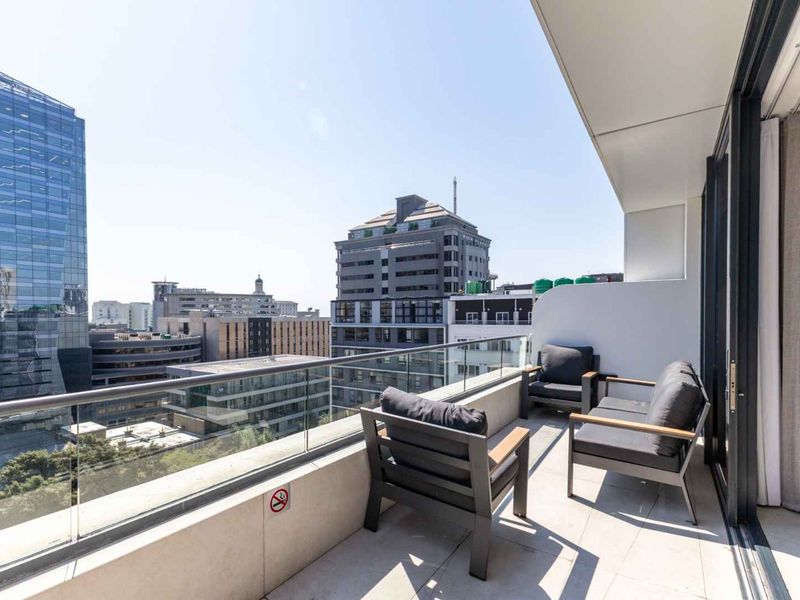 A modern apartment balcony featuring a glass balustrade and tiled flooring, offering an elevated urban city view.