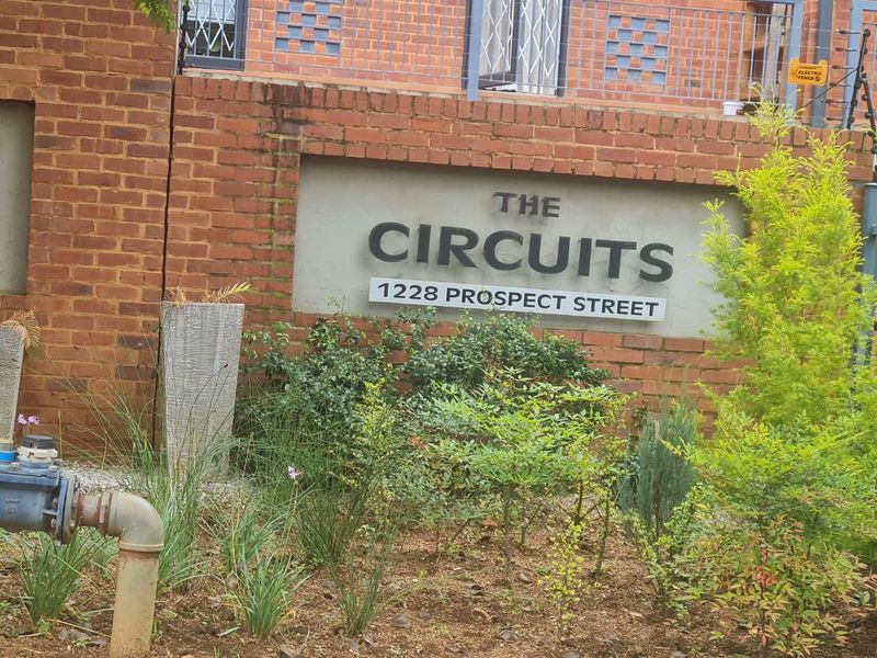 Exterior view of The Circuits apartment complex entrance, featuring brick facade, security electric fencing, and building signage.