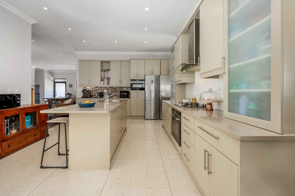 Modern kitchen featuring a central island, stone countertops, built-in oven, gas hob, and ample cabinetry, finished with neutral tiled flooring and recessed lighting.