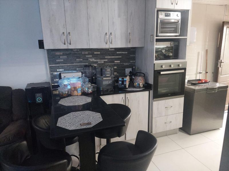 Compact kitchen featuring light wood-grain cabinetry, a dark stone countertop, tiled backsplash, and integrated oven and microwave units.