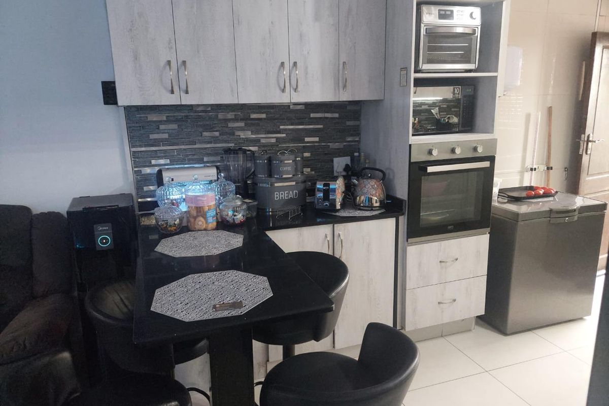 Compact kitchen featuring light wood-grain cabinetry, a dark stone countertop, tiled backsplash, and integrated oven and microwave units.