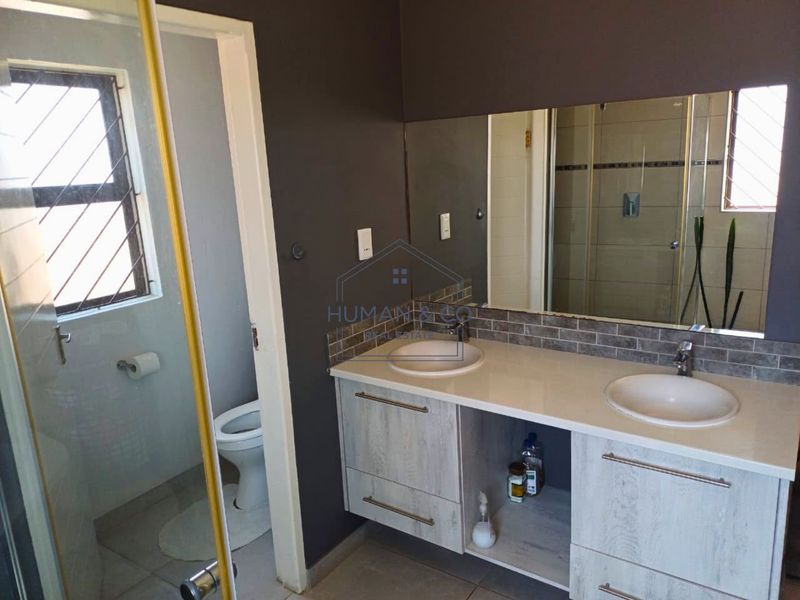 Modern bathroom featuring a double vanity with stone countertop, large wall mirror, tiled splashback, and a separate shower and toilet area.