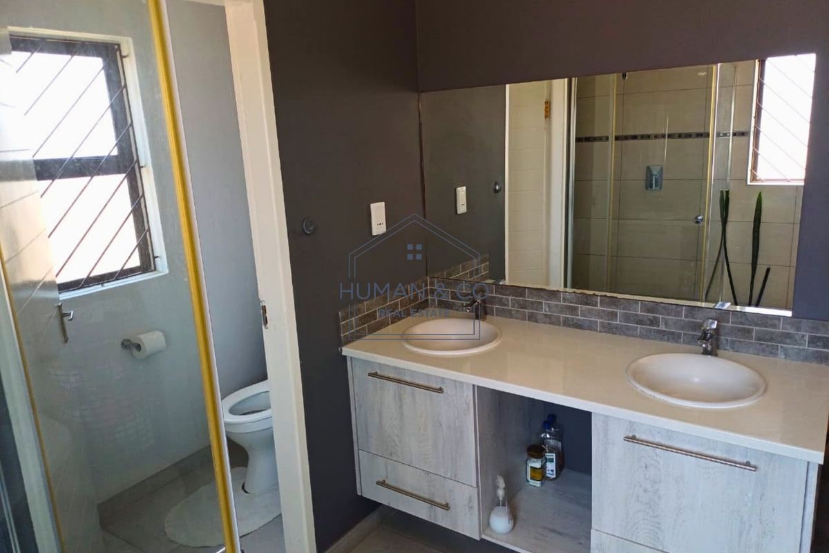 Modern bathroom featuring a double vanity with stone countertop, large wall mirror, tiled splashback, and a separate shower and toilet area.