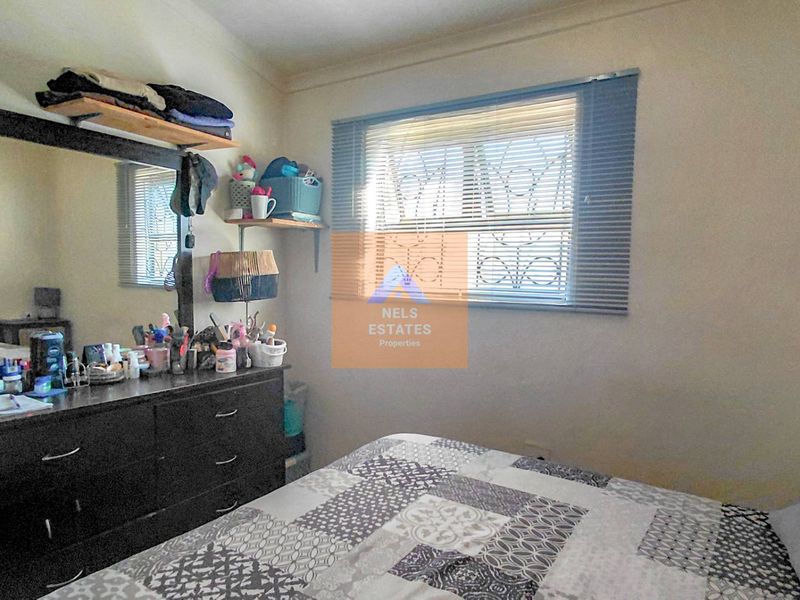 A standard bedroom featuring a window with security bars and fitted venetian blinds.