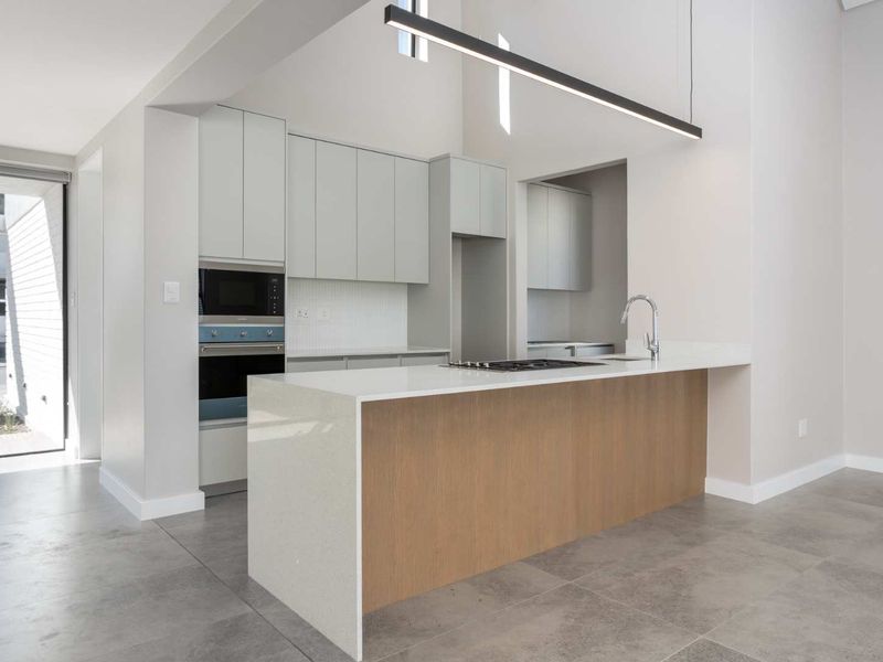 Modern kitchen featuring a central island with quartz countertops, built-in appliances, sleek cabinetry, and high ceilings with contemporary pendant lighting.