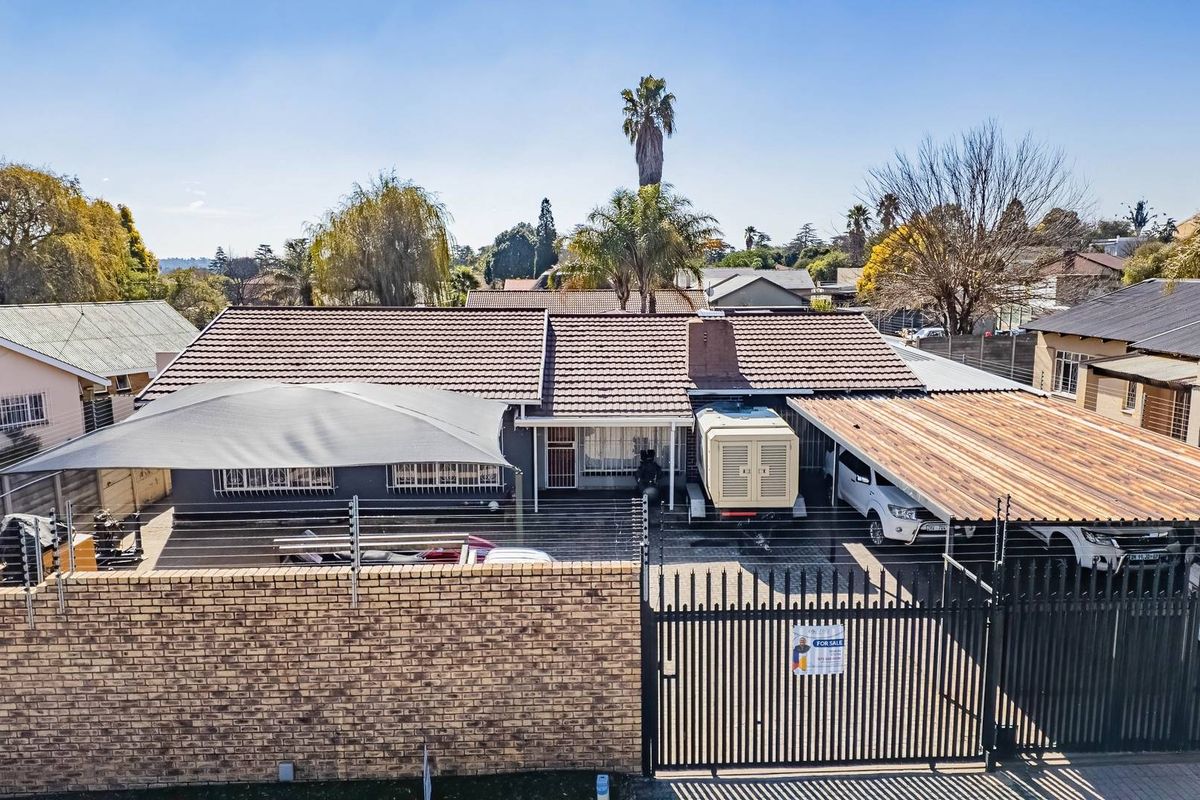 Aerial view of a residential property featuring a tiled roof, double carport, shade sail, perimeter brick wall, and electric fencing.