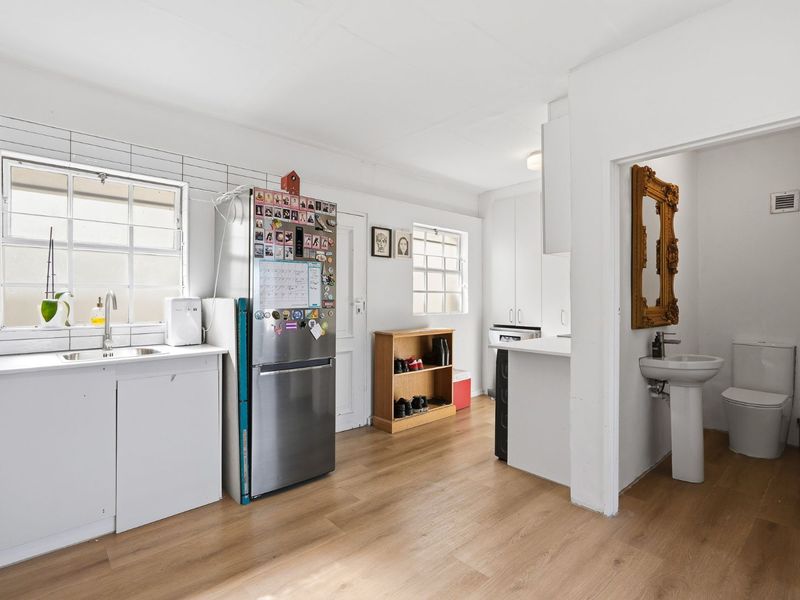 Open plan kitchen area featuring laminate flooring, tiled backsplash, and an adjacent bathroom with a pedestal basin and toilet.