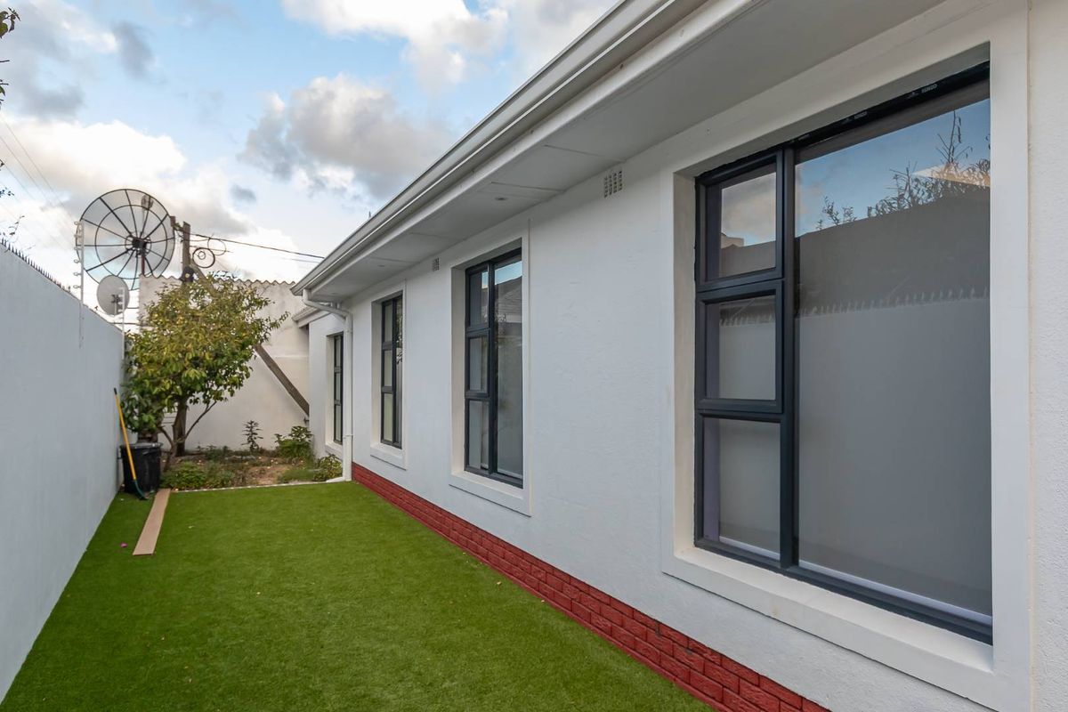 A side exterior view of the house featuring a low-maintenance artificial lawn, white rendered walls, and modern dark-framed windows.