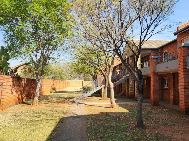 A view of the apartment complex rear exterior, featuring a paved walkway, mature trees, and facebrick building facades with external staircases.