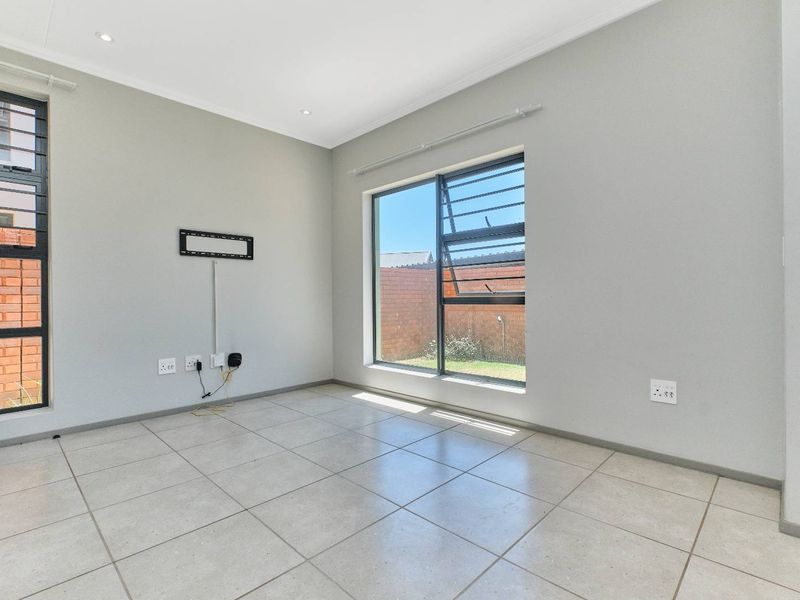 A bright, empty living area featuring neutral tiled flooring, recessed downlighting, and large aluminium-framed windows providing natural light.