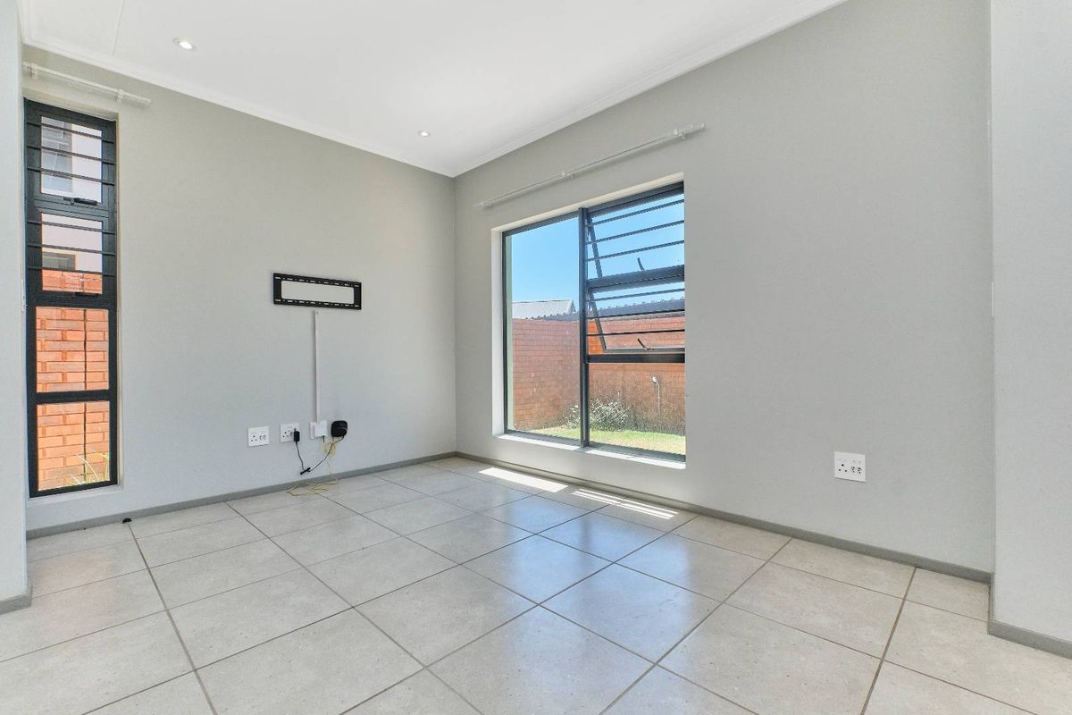 A bright, empty living area featuring neutral tiled flooring, recessed downlighting, and large aluminium-framed windows providing natural light.