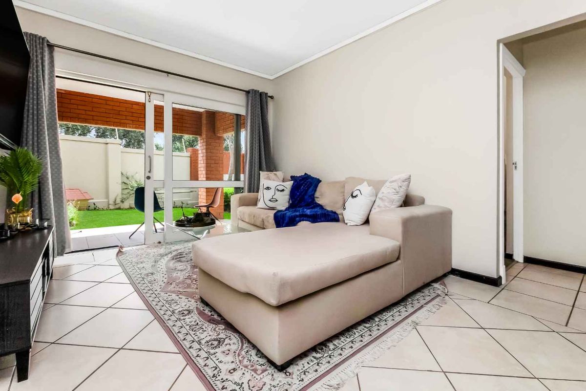 A bright living room featuring tiled flooring and large sliding glass doors that provide direct access to a private patio and garden area.