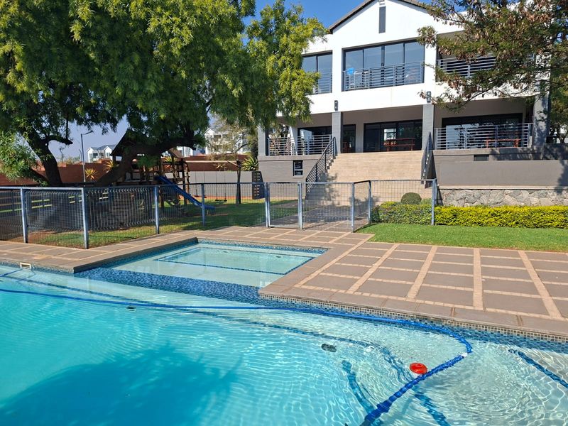 A well-maintained outdoor pool area featuring a paved deck, metal safety fencing, and a clear view of the multi-level residential building facade.