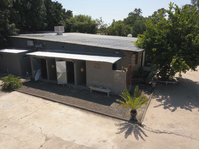 Aerial view of the rear exterior of a single-story building featuring a corrugated metal roof, concrete driveway, and security gates.