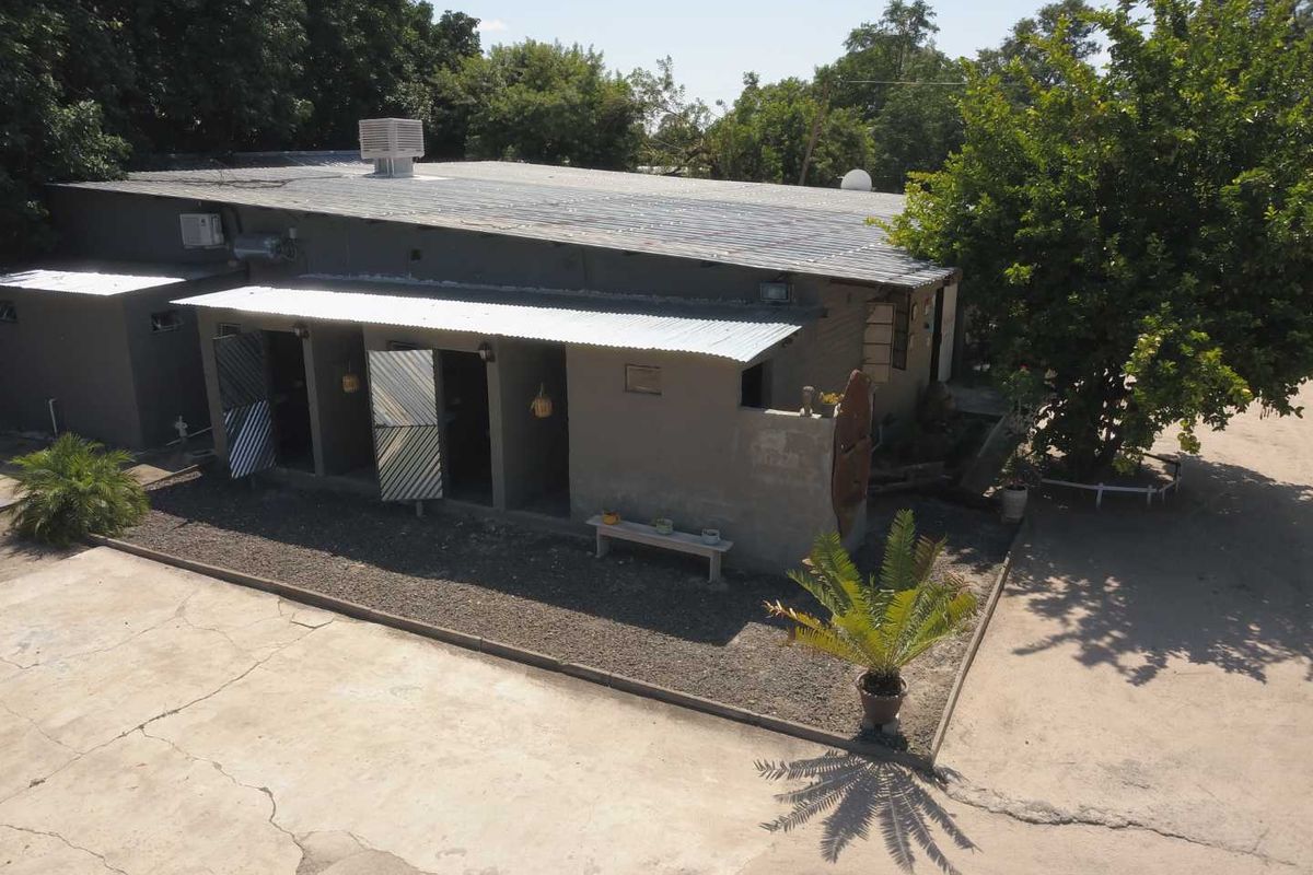 Aerial view of the rear exterior of a single-story building featuring a corrugated metal roof, concrete driveway, and security gates.
