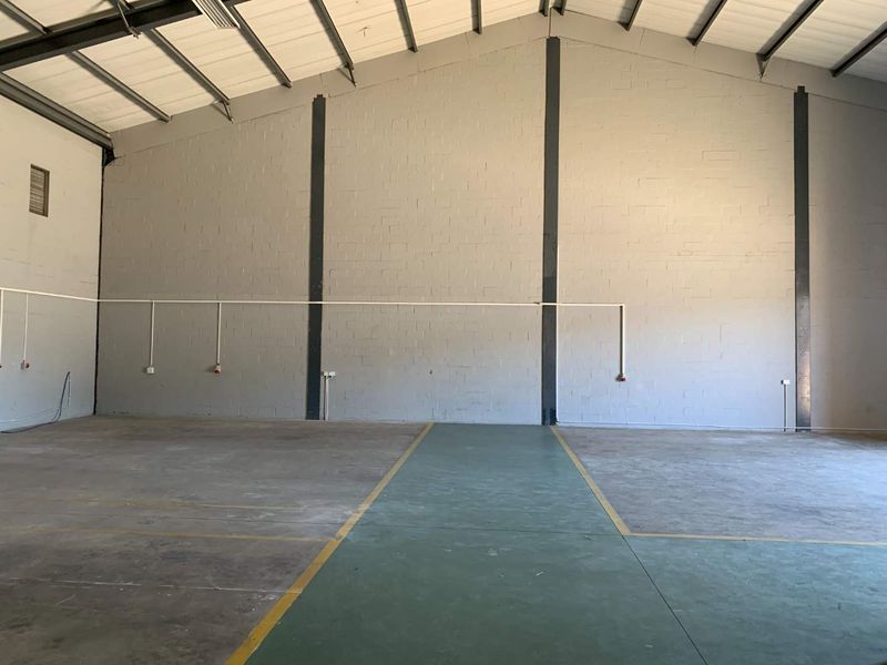 Spacious industrial utility area featuring high ceilings with exposed steel trusses, concrete block walls, and durable painted concrete flooring.