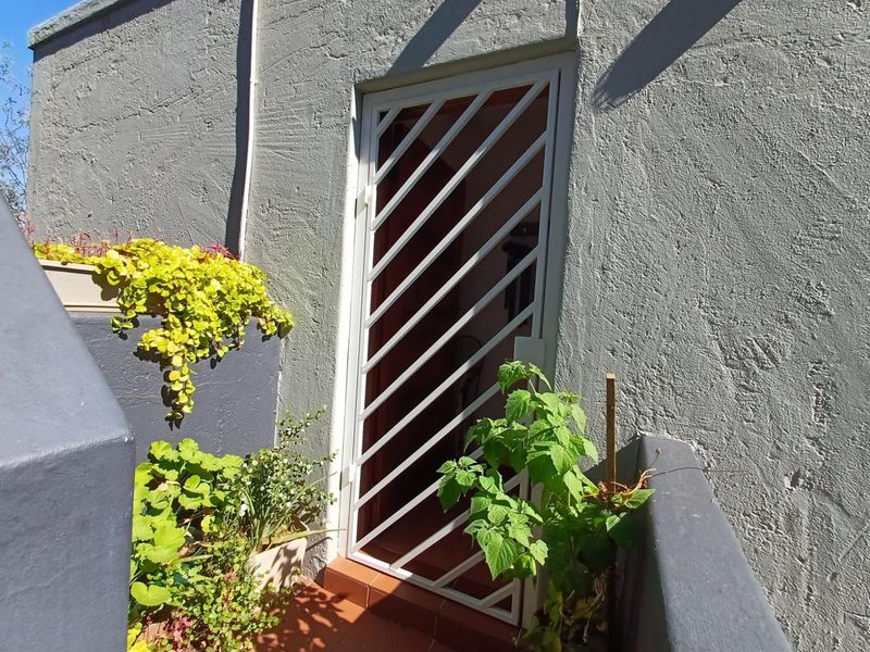 A rear exterior entrance featuring a white security gate and tiled flooring against a textured grey wall.