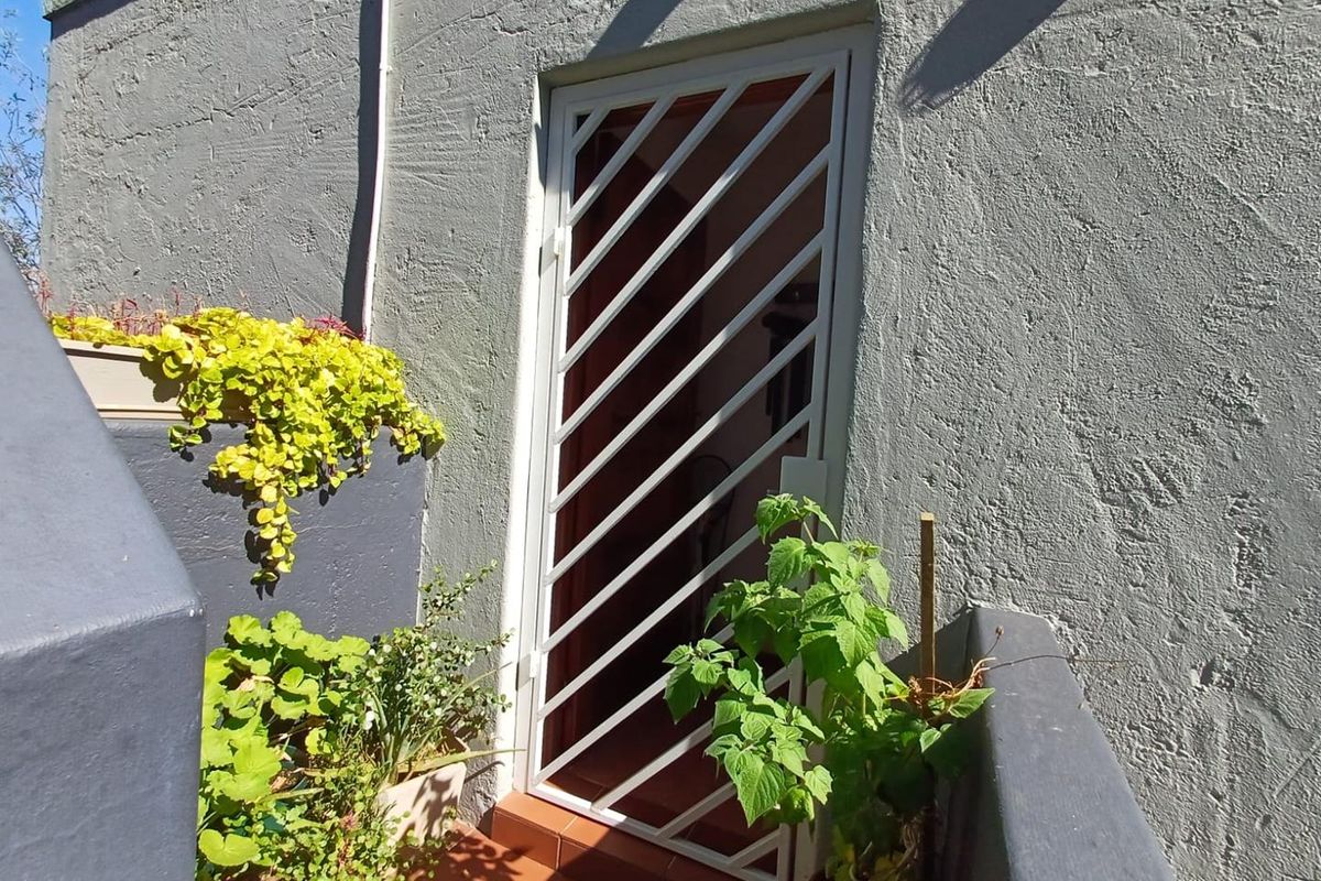 A rear exterior entrance featuring a white security gate and tiled flooring against a textured grey wall.