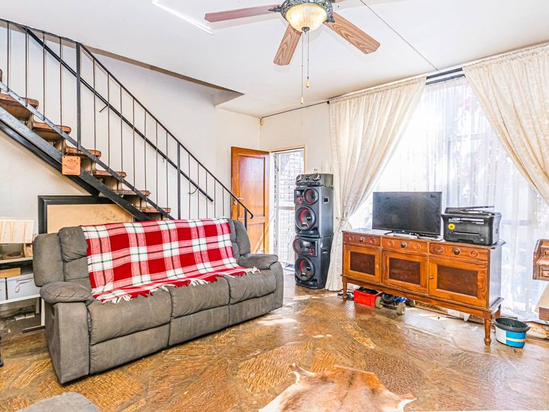 Living room featuring stone flooring, a ceiling fan, and an internal metal staircase leading to the upper level.