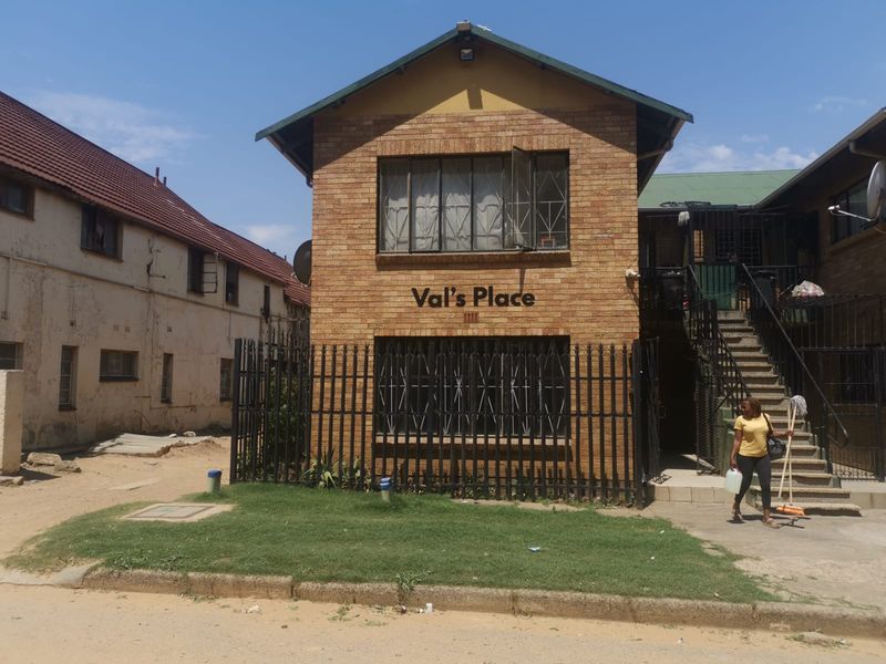 Front elevation of a face brick apartment building featuring metal security bars, an external staircase, and perimeter fencing.