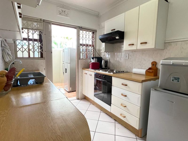 Functional kitchen featuring built-in cabinetry, laminate countertops, integrated oven and hob, tiled backsplash, and direct access to an outdoor area via a sliding door.