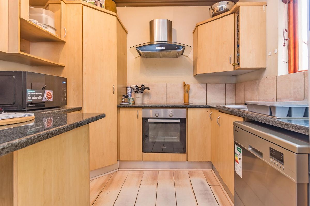 Compact kitchen featuring light wood cabinetry, granite countertops, built-in oven, stainless steel extractor fan, and tiled backsplash.