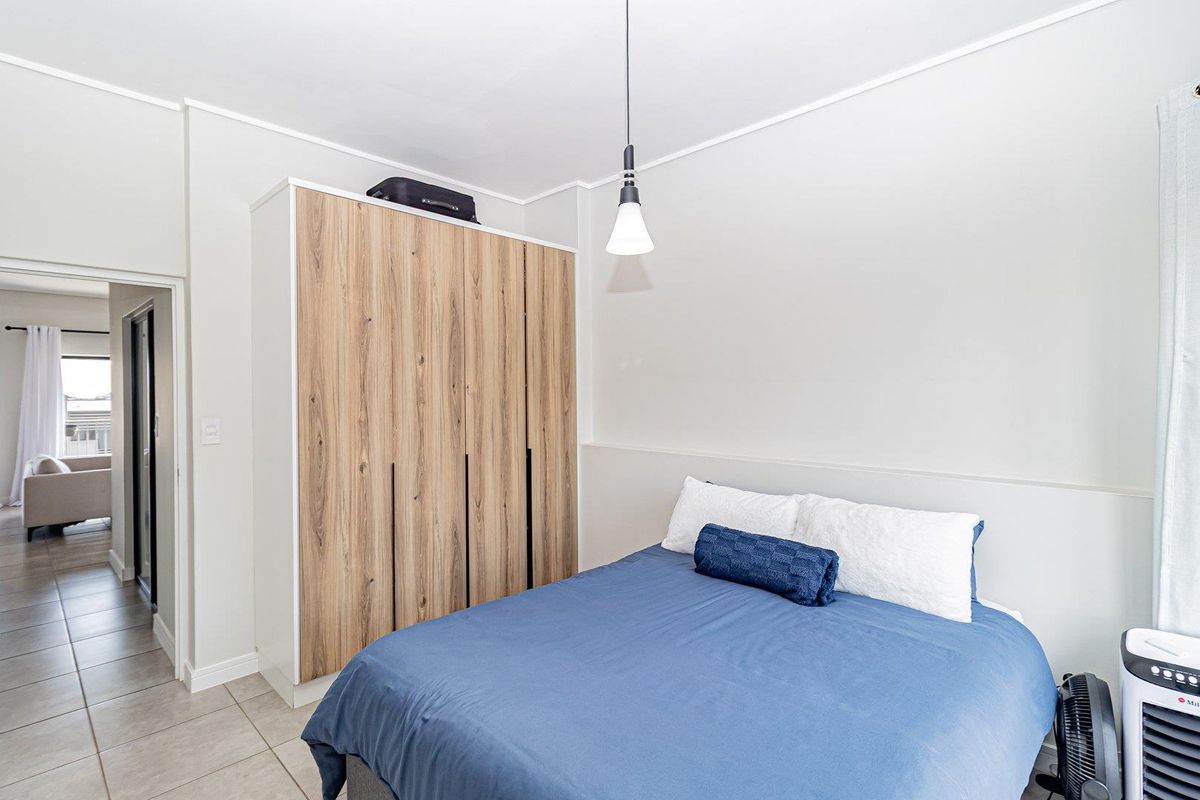 A well-maintained bedroom featuring a modern wood-finish built-in wardrobe, neutral wall tones, and tiled flooring, offering a clean and functional living space.
