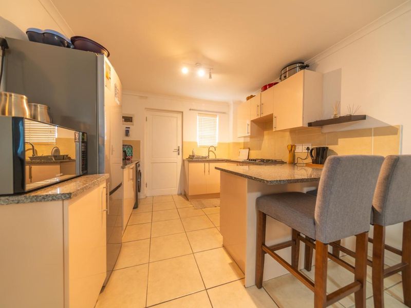 A functional kitchen featuring granite countertops, built-in cabinetry, a gas hob, and tiled flooring, offering a practical layout for daily cooking and meal preparation.