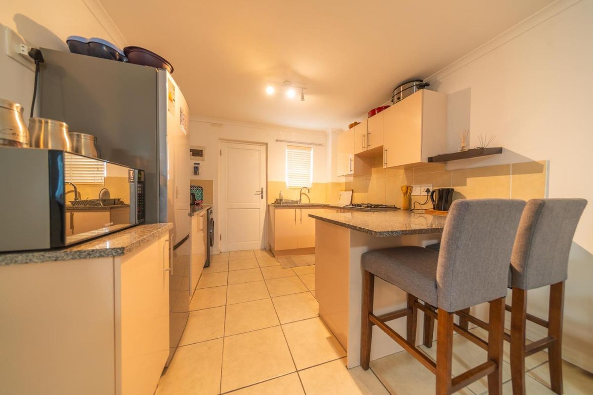 A functional kitchen featuring granite countertops, built-in cabinetry, a gas hob, and tiled flooring, offering a practical layout for daily cooking and meal preparation.