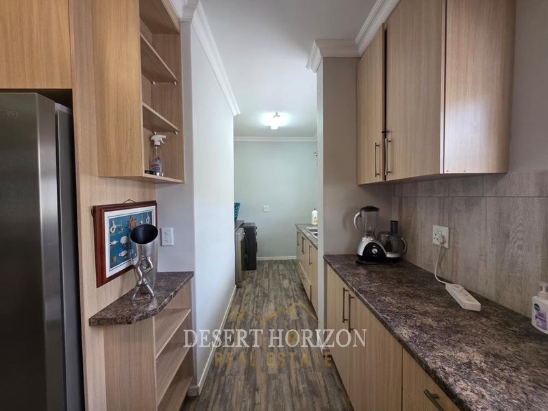 A functional scullery area featuring wood-look laminate cabinetry, durable countertops, and tiled backsplash, providing additional storage and workspace adjacent to the main kitchen.