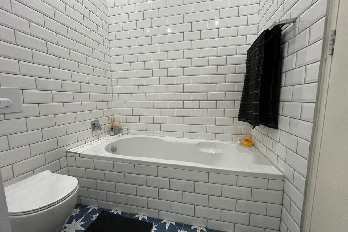 A modern bathroom featuring a built-in bathtub with white subway tile surround, patterned floor tiles, and a wall-mounted toilet.