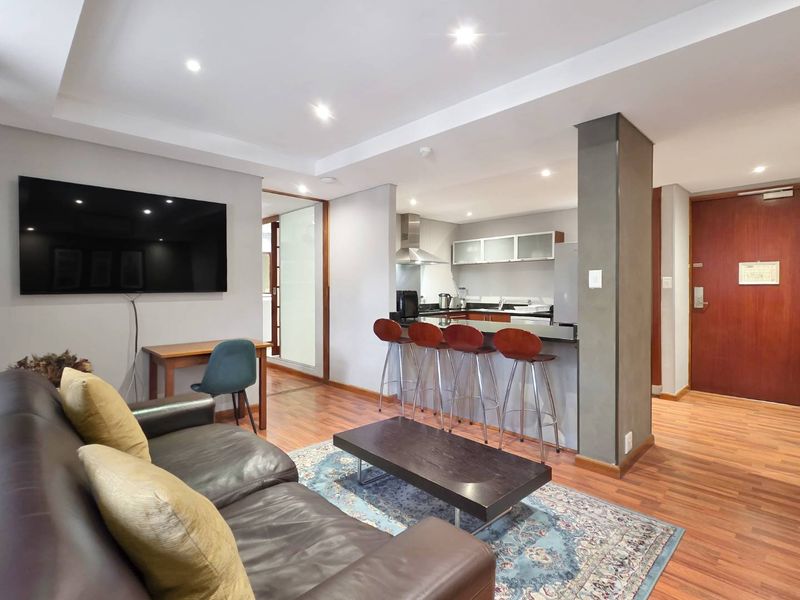 Modern open-plan living area featuring laminate flooring, recessed lighting, and a functional kitchen with a breakfast bar and granite countertops.