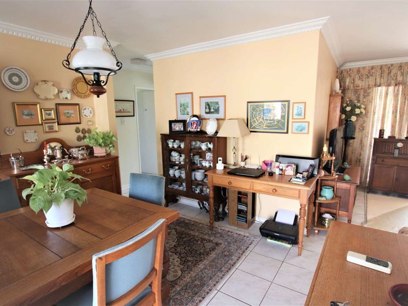 An open-plan living and dining area featuring tiled flooring, crown molding, and a central pendant light, offering a functional and versatile living space.