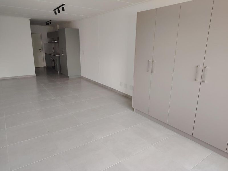 Spacious open-plan living area featuring neutral tiled flooring, modern built-in cupboards, and a compact kitchen with integrated appliances.