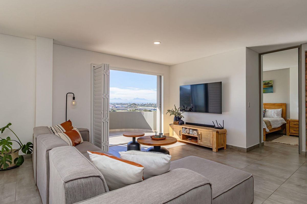 Modern living area featuring tiled flooring, a striking exposed brick feature wall, and seamless access to a balcony with scenic mountain views.