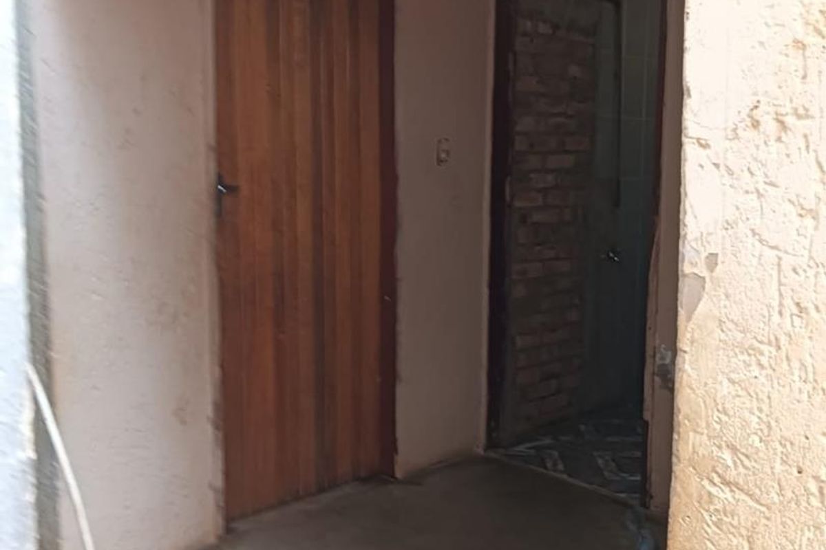An exterior entrance area showing significant wear, including peeling paint, exposed brickwork, and unfinished door frames requiring maintenance and repair.