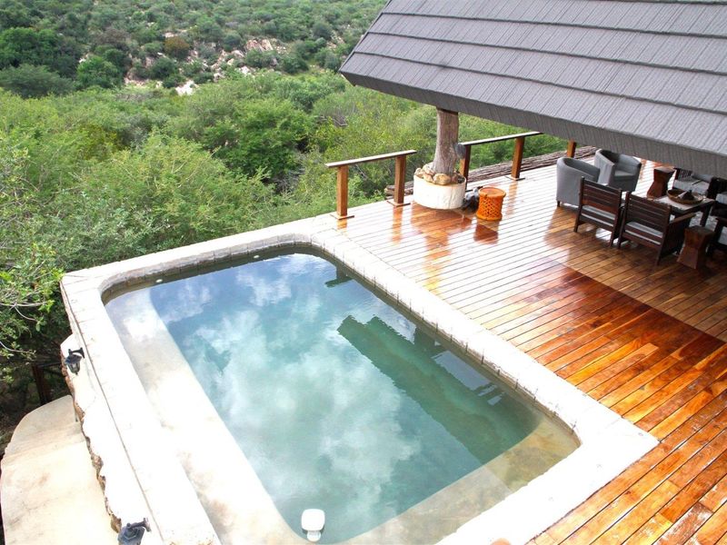An elevated outdoor pool area featuring timber decking, a covered patio space, and scenic views of the surrounding natural landscape.