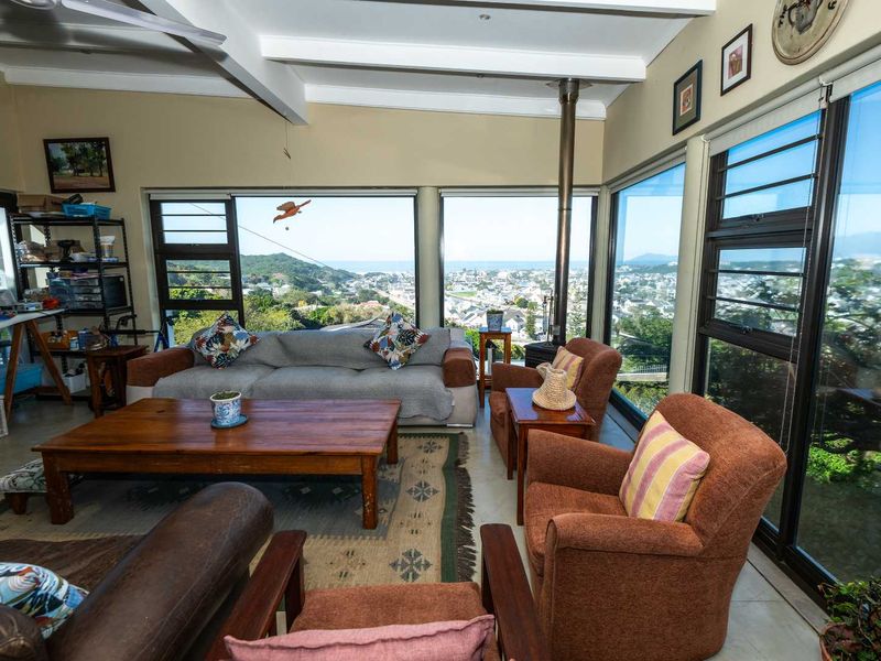Spacious living area featuring a wood-burning fireplace, exposed ceiling beams, and expansive windows offering panoramic coastal and neighborhood views.