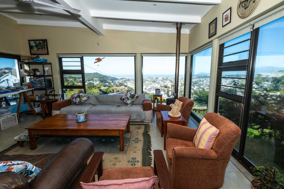 Spacious living area featuring a wood-burning fireplace, exposed ceiling beams, and expansive windows offering panoramic coastal and neighborhood views.
