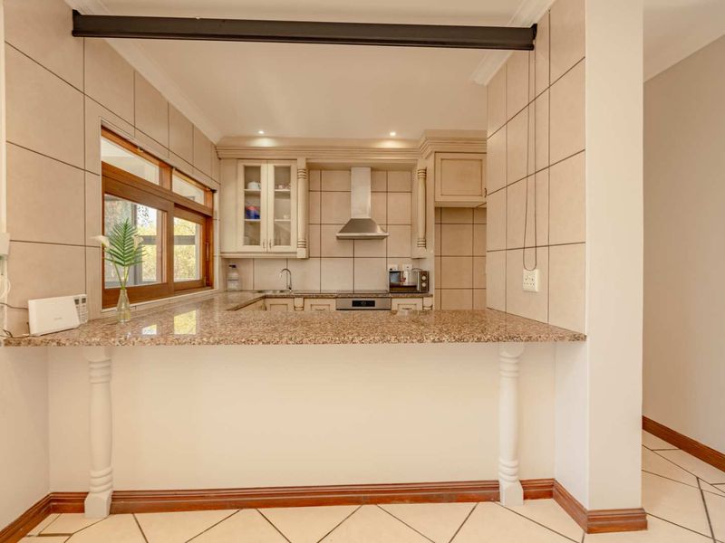 A functional kitchen featuring granite countertops, built-in cabinetry, a stainless steel extractor fan, and a breakfast bar, finished with neutral wall and floor tiles.