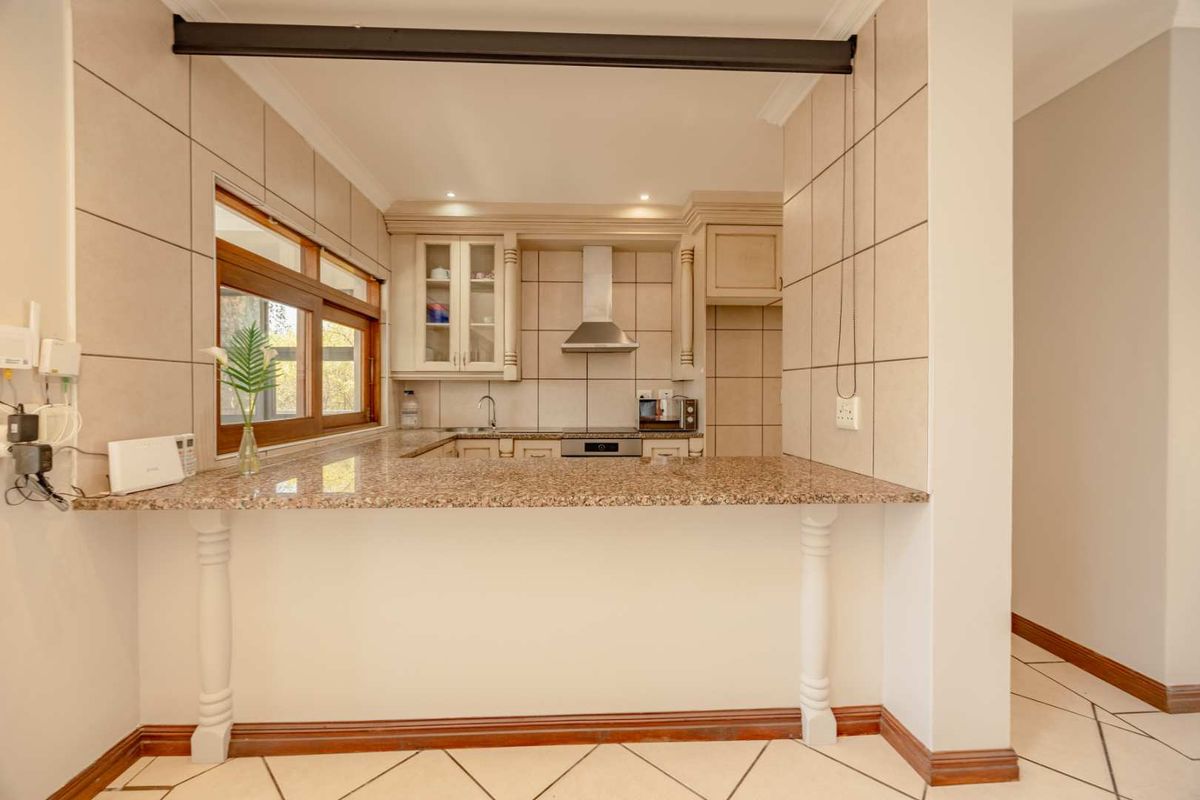 A functional kitchen featuring granite countertops, built-in cabinetry, a stainless steel extractor fan, and a breakfast bar, finished with neutral wall and floor tiles.