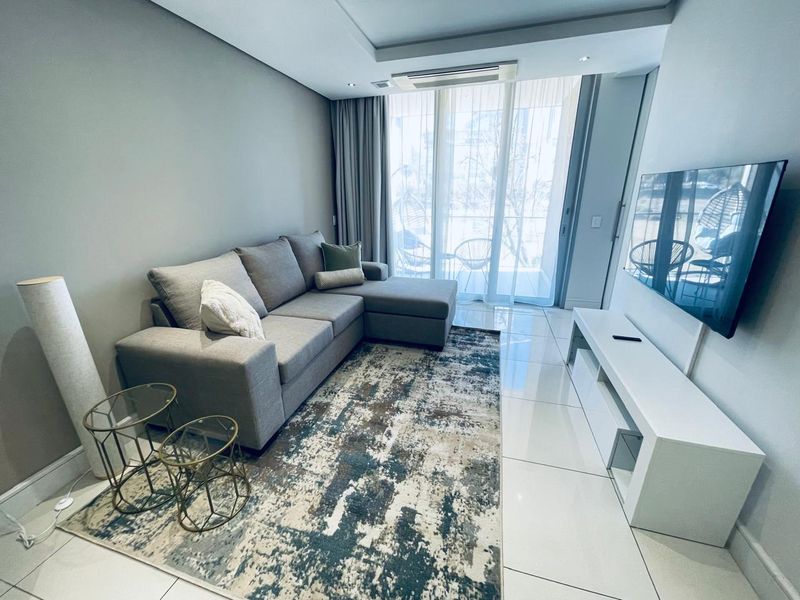 A modern, well-maintained living room featuring sleek tiled flooring, recessed ceiling lighting, and a large sliding glass door providing access to the balcony.