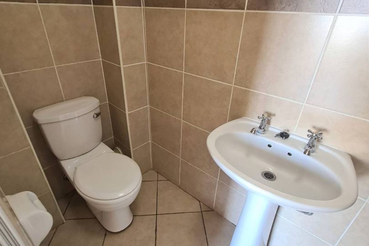 A functional bathroom featuring a pedestal basin, toilet, and neutral ceramic wall and floor tiling.
