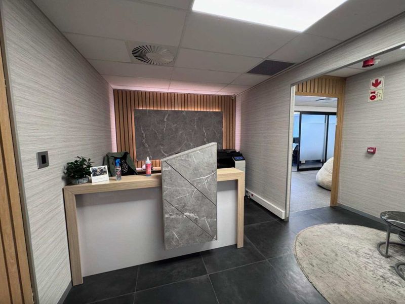 Modern office reception area featuring a contemporary built-in desk, slatted wood accent wall, and professional tiled flooring with access to adjacent office space.
