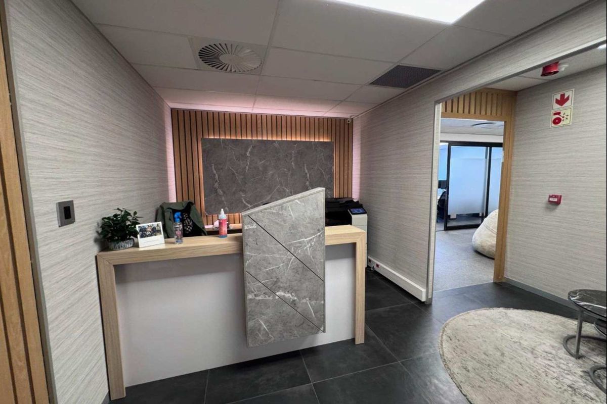 Modern office reception area featuring a contemporary built-in desk, slatted wood accent wall, and professional tiled flooring with access to adjacent office space.