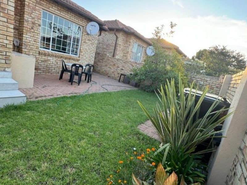 A rear view of the townhouse featuring a face brick facade, a paved patio area, and a private garden with a boundary wall.