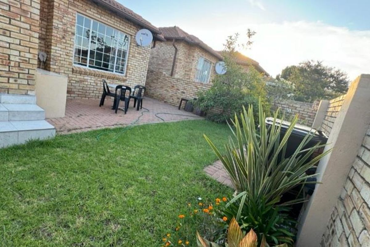 A rear view of the townhouse featuring a face brick facade, a paved patio area, and a private garden with a boundary wall.
